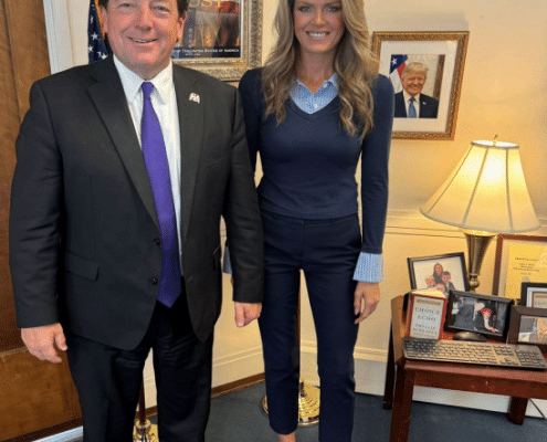 Ed Martin and Lindsey Halligan posing together in his office. They both look really weird, with him being bottom-heavy and forward leaning,and her propped up on ugly shoes.