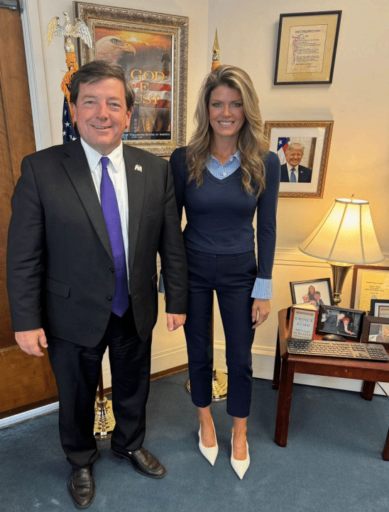 Ed Martin and Lindsey Halligan posing together in his office. They both look really weird, with him being bottom-heavy and forward leaning,and her propped up on ugly shoes.